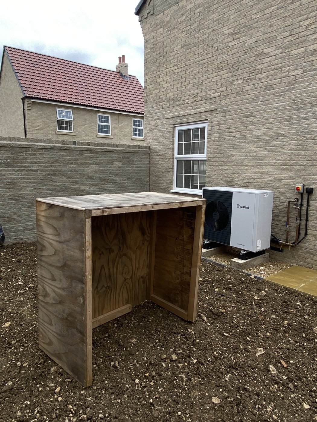 Homemade plywood box standing beside an uncovered heat pump