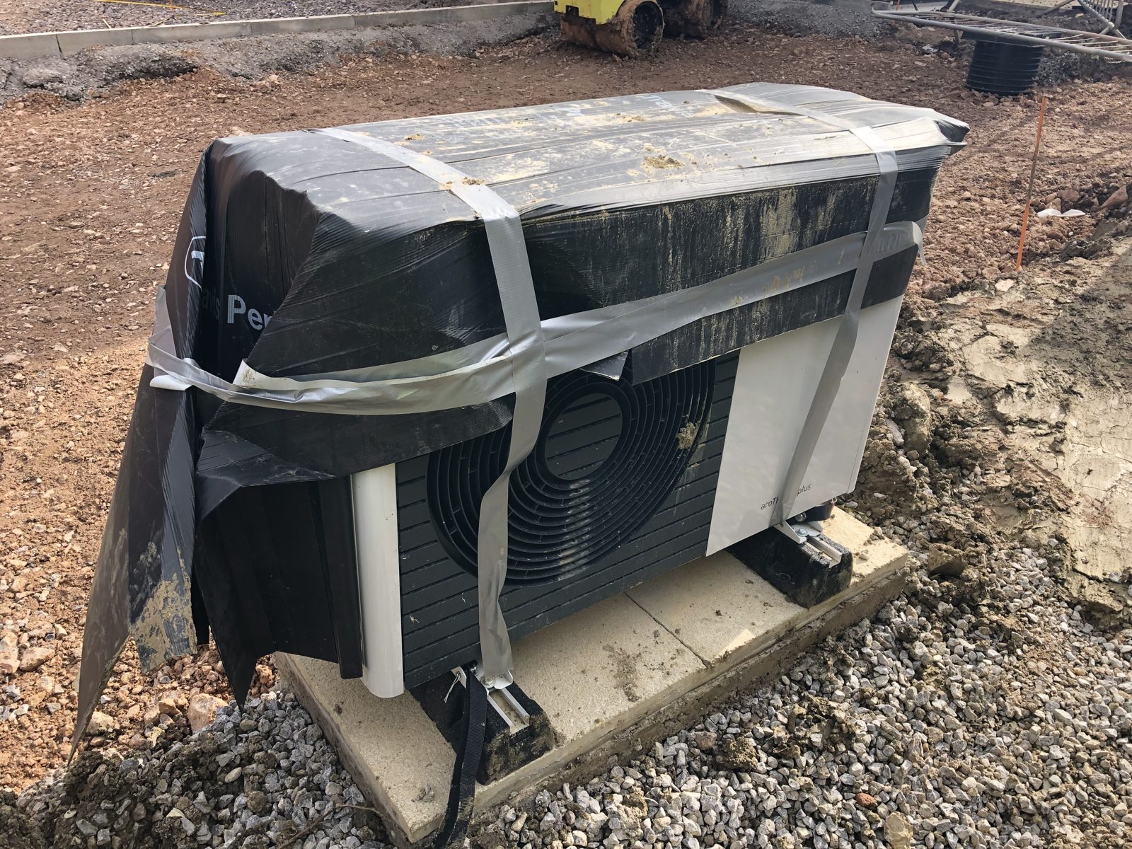 Heat pump wrapped in black plastic sheeting and tape on a building site
